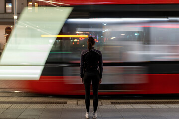 Caucasian lady waiting public transport light rail tram long exposure red yellow