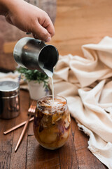 Barista pouring milk into a glass of iced coffee
