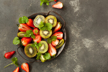 bright and fresh strawberries and kiwi scattered in handfuls on a dark background