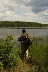 Naklejka premium Fishing in river. A fisherman with a fishing rod on the river bank. Man fisherman catches a fish pike. Fishing, spinning reel, fish - The concept of a rural getaway. Article about fishing. 