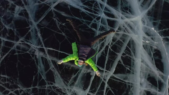  Aerial view of a drone taking off. A girl lies on the ice in winter in warm clothes and waves her arms and legs to the side, depicting an angel