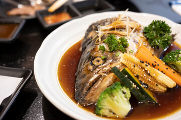 Salmon kabutoni with Japanese style sauce and boiled vegetables on white dish.