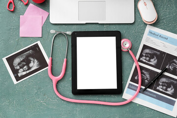 Tablet computer with stethoscope, ultrasound image of baby and accessories of obstetrician on color...