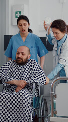 Obraz premium Medical team helping sick patient with leg fracture putting in wheelchair going on physiotherapy recovering in hospital ward. Doctor consulting patient checking respiratory expertise