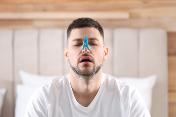 Man with clothespin suffering from runny nose in bedroom - obrazy, fototapety, plakaty