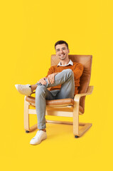 Fototapeta na wymiar Young man sitting in armchair on color background