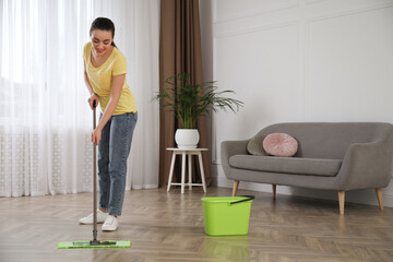 Young woman cleaning floor with mop in living room