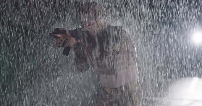 Close-up heavy raindrops on soldier in camouflage on the night, taking military action, aiming weapon sight, and looking straight ahead powerfully and calmly