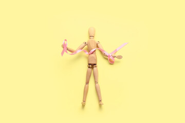 Wooden mannequin with pink ribbon on color background. Breast cancer concept