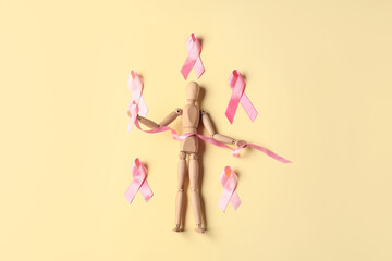 Fototapeta premium Wooden mannequin with pink ribbons on color background. Breast cancer concept