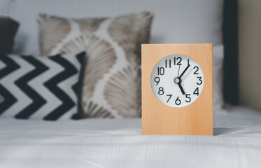A wooden framed alarm clock is placed on the left hand side. The background is a soft focus pillow that is lined up.