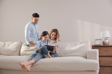 Family with little daughter using tablet on sofa in living room