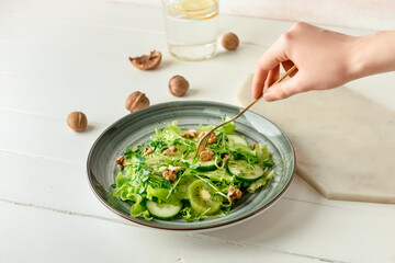 Woman eating fresh salad on light wooden background