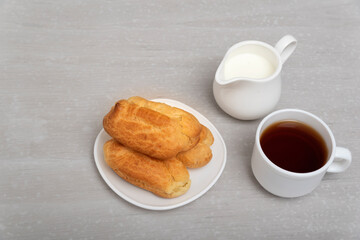 Homemade eclairs, coffee and milk. Traditional French eclairs. Profiteroles on saucer. Gray background