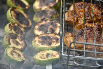 Delicious grilled zucchini skewers in the fire smoke and chicken meat with golden crust.
