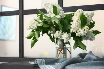 Vase with lilac flowers on table near window