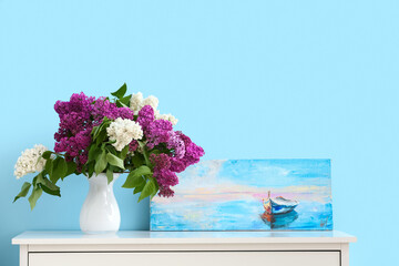 Vase with lilac flowers and painting on shelf near color wall