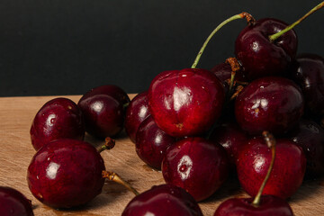 Pile of fresh cherries on wooden desk, black background.