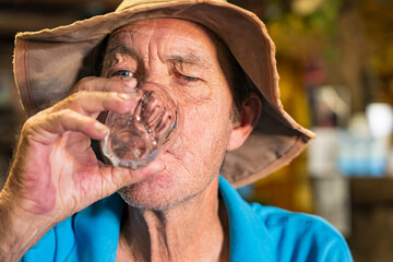 An elderly man wearing a hat drinking from a glass in a pub