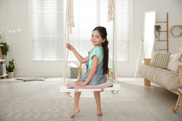 Cute little girl playing on swing at home