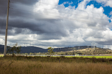 Wind turbines on hill above paddock with solar farm with cloudy sky and power lines