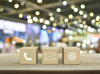 Telephone, mail, email address icon on wood block cubes on wooden table over blur light and shadow...