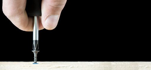 Banner with screwdriver twists the self-cut into wooden boards close up isolated on black background with space for text.