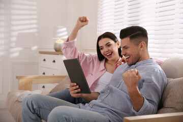 Emotional couple participating in online auction using tablet at home - obrazy, fototapety, plakaty