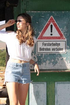 Eine junge Frau in sexy Shorts steht an einer Hütte neben Verkehrsschild