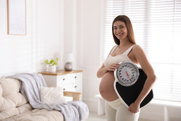 Young pregnant woman with scales at home. Space for text