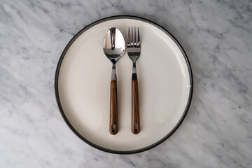 spoon and fork on empty plate on marble table