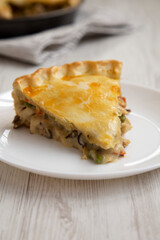 A Piece of Chicken Pot Pie on a white plate on a white wooden background, side view.