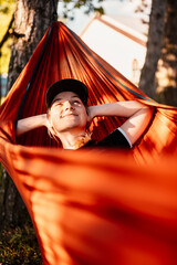 Woman with cap resting in comfortable hammock during sunset. Relaxing on orange hammock between two...