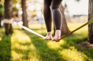 Foto op Canvas Slacklining is a practice in balance that typically uses nylon or polyester webbing. Girl walking on a slackline in a park during a sunset. Slack line © alexanderuhrin