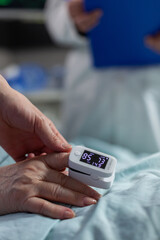 Close up of oxymeter attached on patient laying in hospital bed, indicating oxygen saturation...