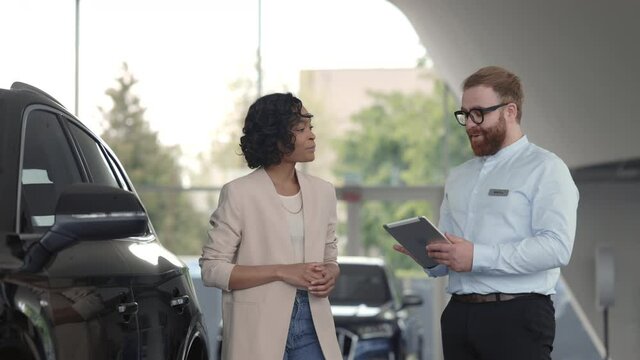 Salesman with tablet presenting car to female client