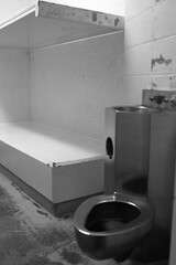 Vertical shot of a stainless steel toilet bowl and sink inside a prison cell