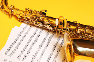 Beautiful saxophone and note sheets on yellow background, closeup