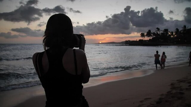 Woman taking a photo on the beach at sunset in Poipu Beach, Kauai, Hawaii. Mid angle, parallax movement, slow motion, HD.