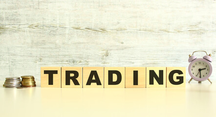 There are seven wooden cubes with letters on the table next to the coins. TRADING word. On a gray background.