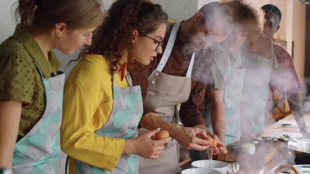Professional male chef in apron teaching young woman how to separate egg white and yolk during cooking master class