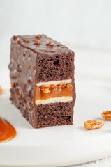 Snickers cake. Dessert based on chocolate biscuit, creamy mousse with caramel. Decorated with caramelized peanuts. On a white plate. Light background. Close-up. Macro.