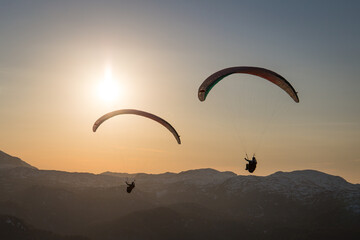 Paragliding couple flying in sunset over the mountains