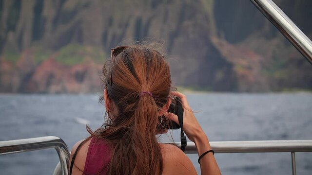 Woman photographing dramatic Na Pali Coast from boat at sea in Kauai, Hawaii. Mid angle, parallax movement, HD.