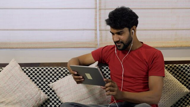 Young Asian man smiling,using digital tablet for internet and social media.Happy guy holding PC tablet for movies and watching funny videos.Indian guy watching funny film and on tablet.lifestyle.
