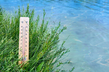 Weather thermometer in the grass on the blue water background