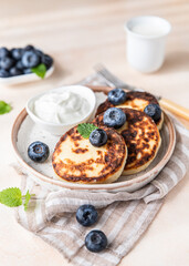Fried cottage cheese pancakes or fritters with blueberry and sour cream on a plate. Gluten free. Traditional breakfast of Ukrainian and Russian cuisine.