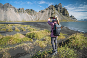Naklejka premium Woman hiker with backpack at black sand dunes on the Stokksnes headland on southeastern Icelandic coast with Vestrahorn. Europe.