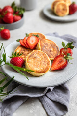 Cottage cheese pancakes or fritters with strawberry and natural yogurt on light grey stone background. Healthy breakfast or lunch. Syrniki.