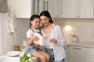 Little daughter congratulating her mom in kitchen at home. Happy Mother's Day